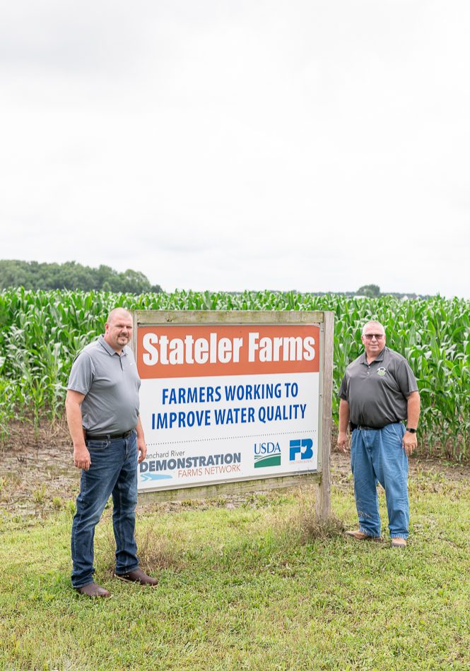 Stateler Farm farmers standing by Stateler Farm sign
